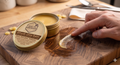 Billiards glide balm being applied to a wooden surface with a tin of balm and a hand holding a small amount.
